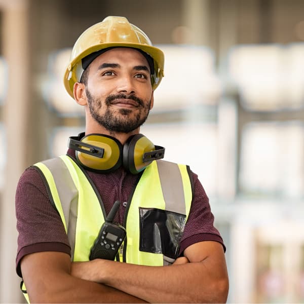 Construction worker wearing hard hat, high visibility vest and ear protection standing confidently on an industrial site